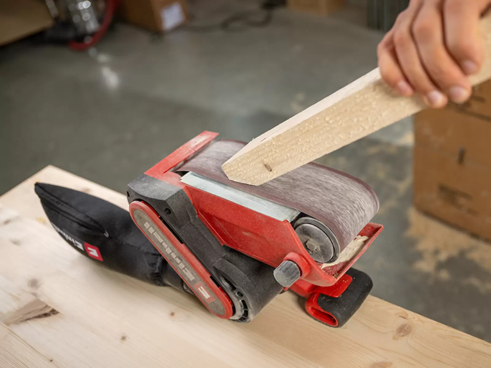 Une personne ponce un morceau de bois à l’aide de la ponceuse à bande Einhell TC-BS 800, fixée à un établi.