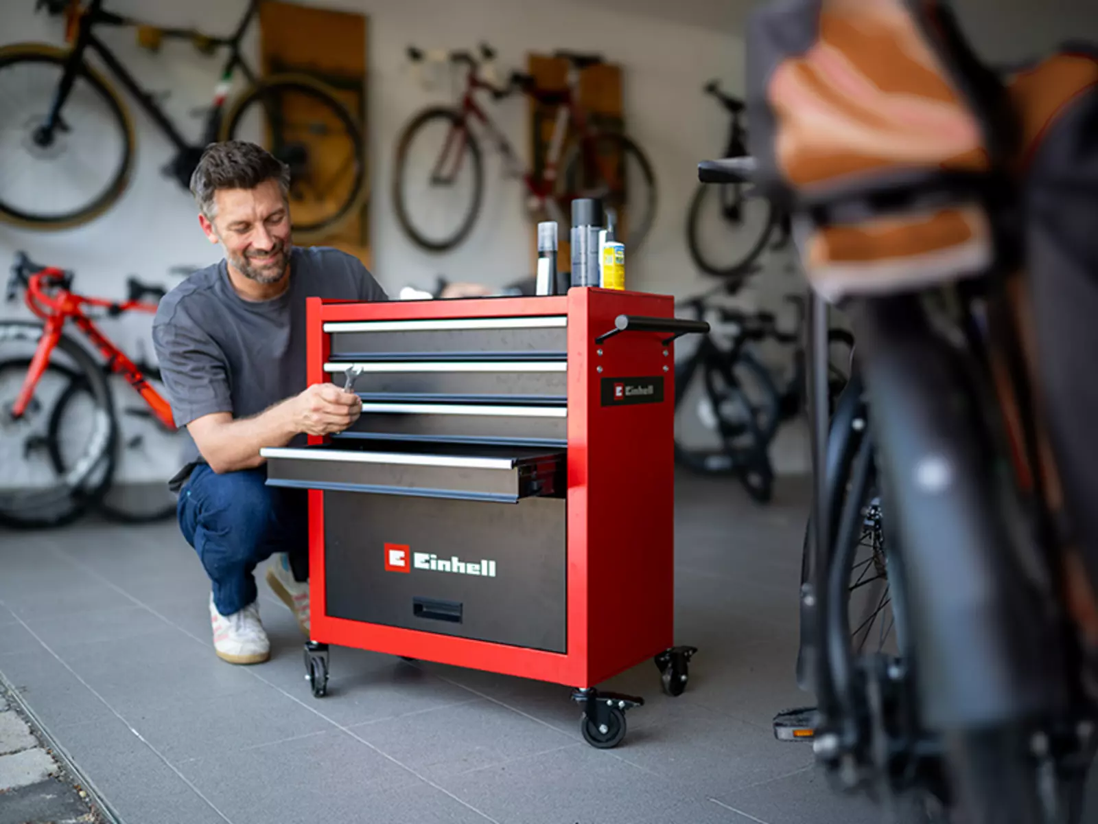 Ein Mann öffnet eine Schublade des Einhell Werkstattwagens TC-TW 100 in einer Garage mit mehreren Fahrrädern.