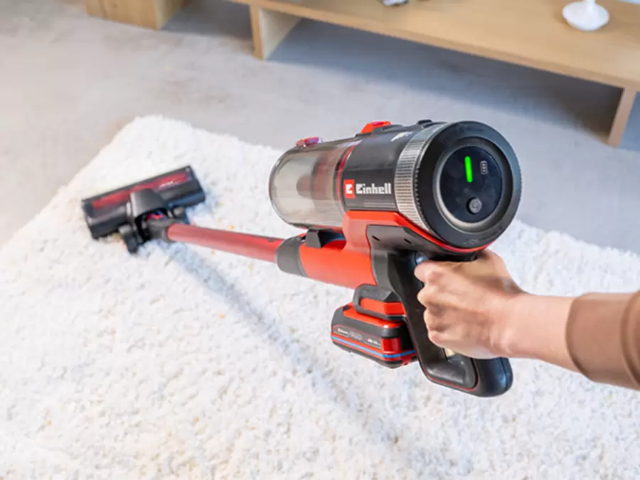 A person guides the Einhell cordless stick vacuum cleaner TE-SV 18/270/1 Li BL-Solo with one hand while vacuuming a carpet.