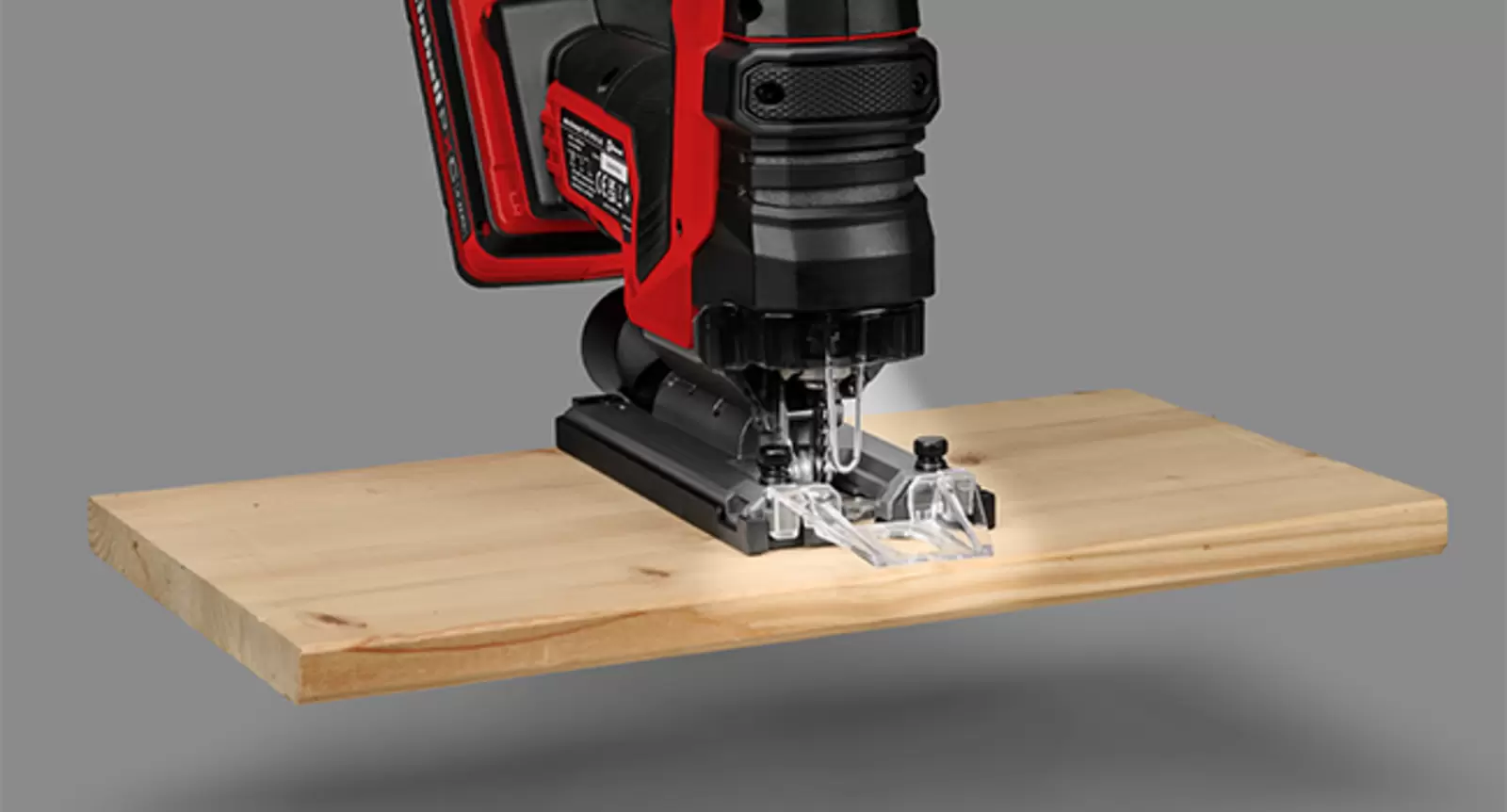 Einhell Professional cordless jigsaw being used to make a precise cut in a wooden board, illuminated by the integrated LED light at the cutting area.