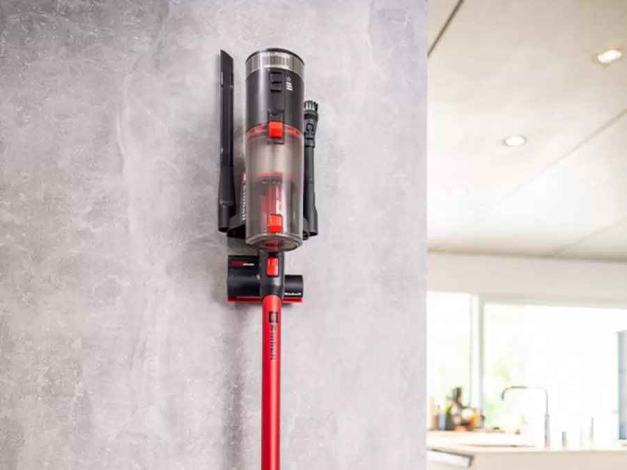 The Einhell cordless stick vacuum cleaner TE-SV 18/270/1 Li BL-Solo is mounted on a wall with its accessories.
