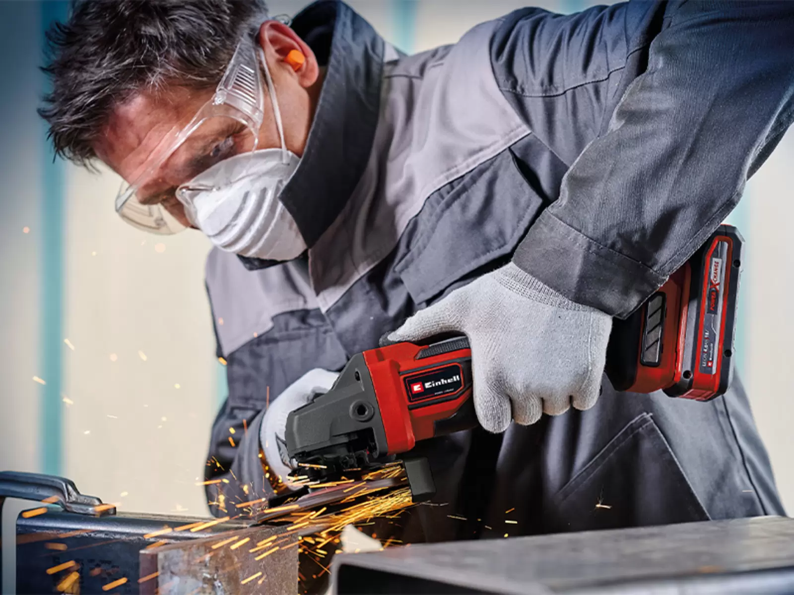 A person uses the Einhell Cordless Angle Grinder TP-AG 18/125 CE +3 Set - Solo on a metal piece, with sparks flying.