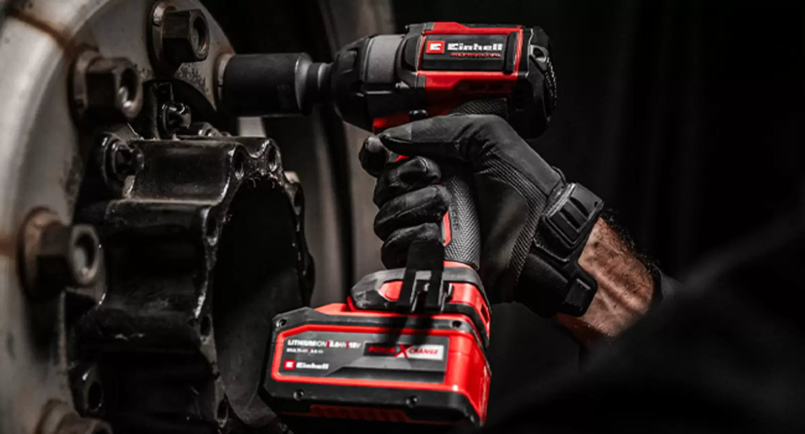 A man with gloves loosens a wheel nut on a large vehicle wheel with the Einhell Professional cordless impact wrench TP-CWD 18/7501-C Li BL +6 S-F.