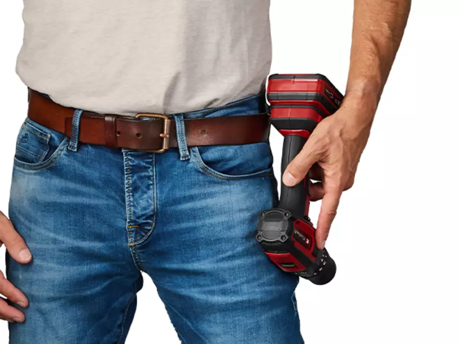 Um homem usa o Einhell berbequim de impacto a bateria TE-CD 18/52 Li-i no clipe de cinto preso ao jeans.