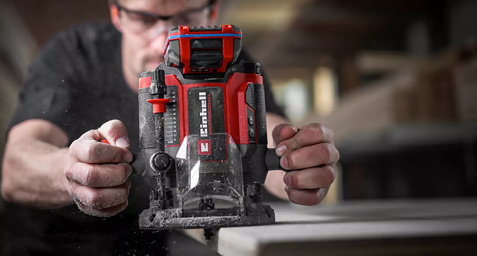 Die Einhell Akku-Oberfräse TP-RO 18/55 Li BL - Solo beim Arbeiten auf einer Holzplatte, Hand stellt die Frästiefe ein.