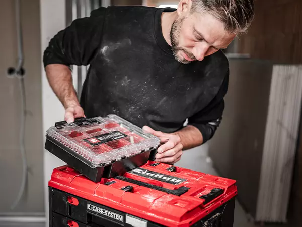 A person carrying a filled Einhell E-Case Half-size organiser box with clear lid and visible Einhell logo.