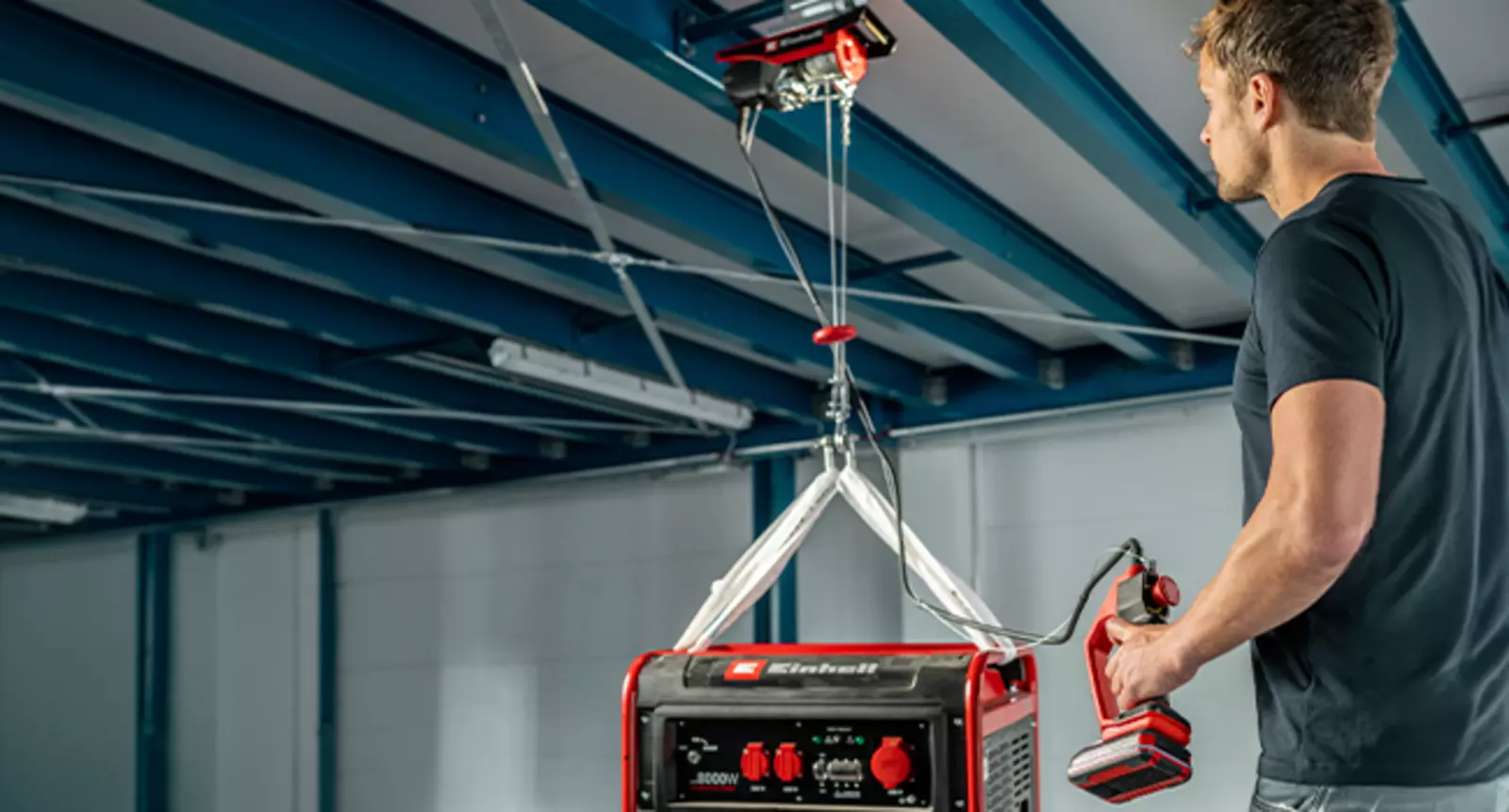 Einhell akülü halatlı vinç TE-EH 18/250 Li BL, bir erkek tarafından kontrol edilen bir salonda bir jeneratörü kaldırır.