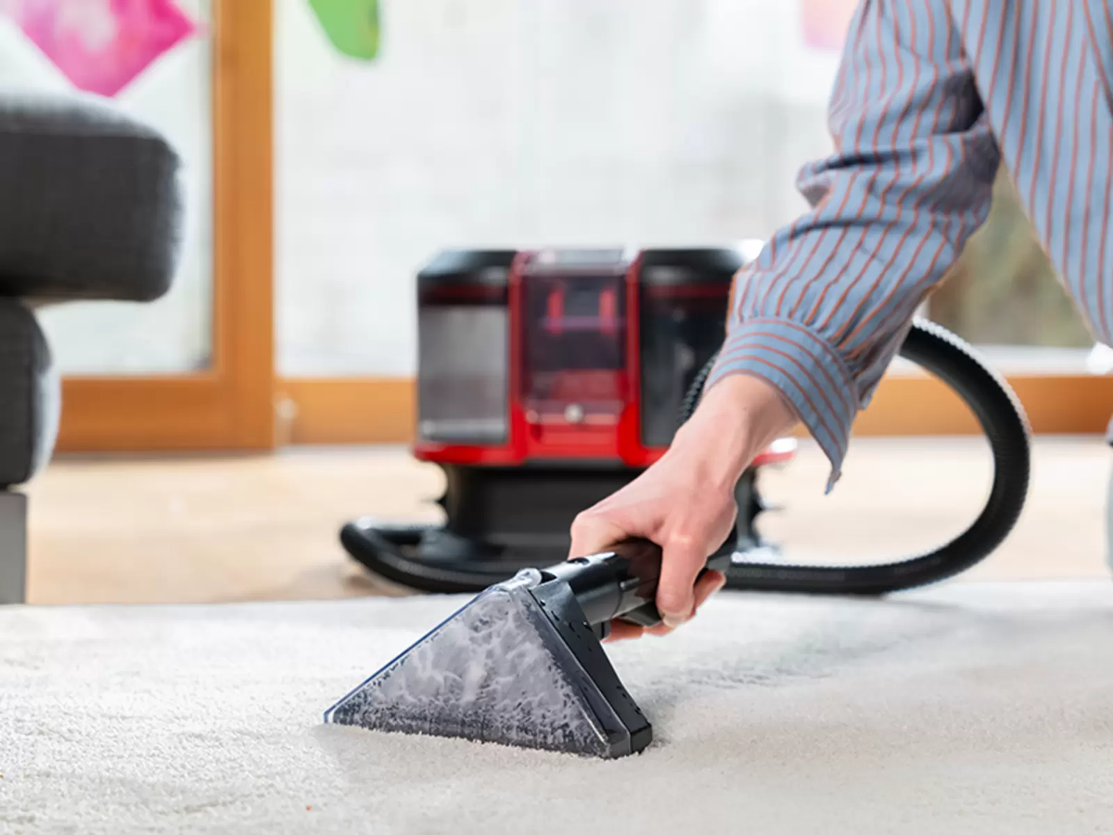 Eine Person reinigt einen hellen Teppich mit dem Einhell Akku-Waschsauger TE-SCL 18/1100 Li-S BL-Solo.