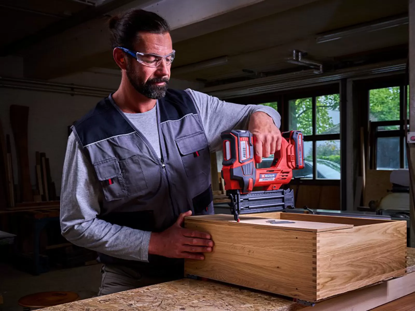 Ein Mann arbeitet in einer Werkstatt mit dem Einhell Akku-Nagler FIXETTO 18/50 N S-F und befestigt Nägel in einem Holzrahmen.