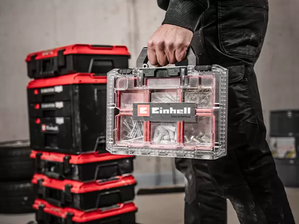Person carrying a loaded Einhell Pro System Half Size Organiser Case with a transparent lid and visible Einhell branding.