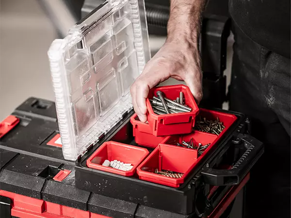 Opened Einhell E-Case Half-size organiser box with red inserts holding screws and dowels; a compartment is being taken out by a hand.