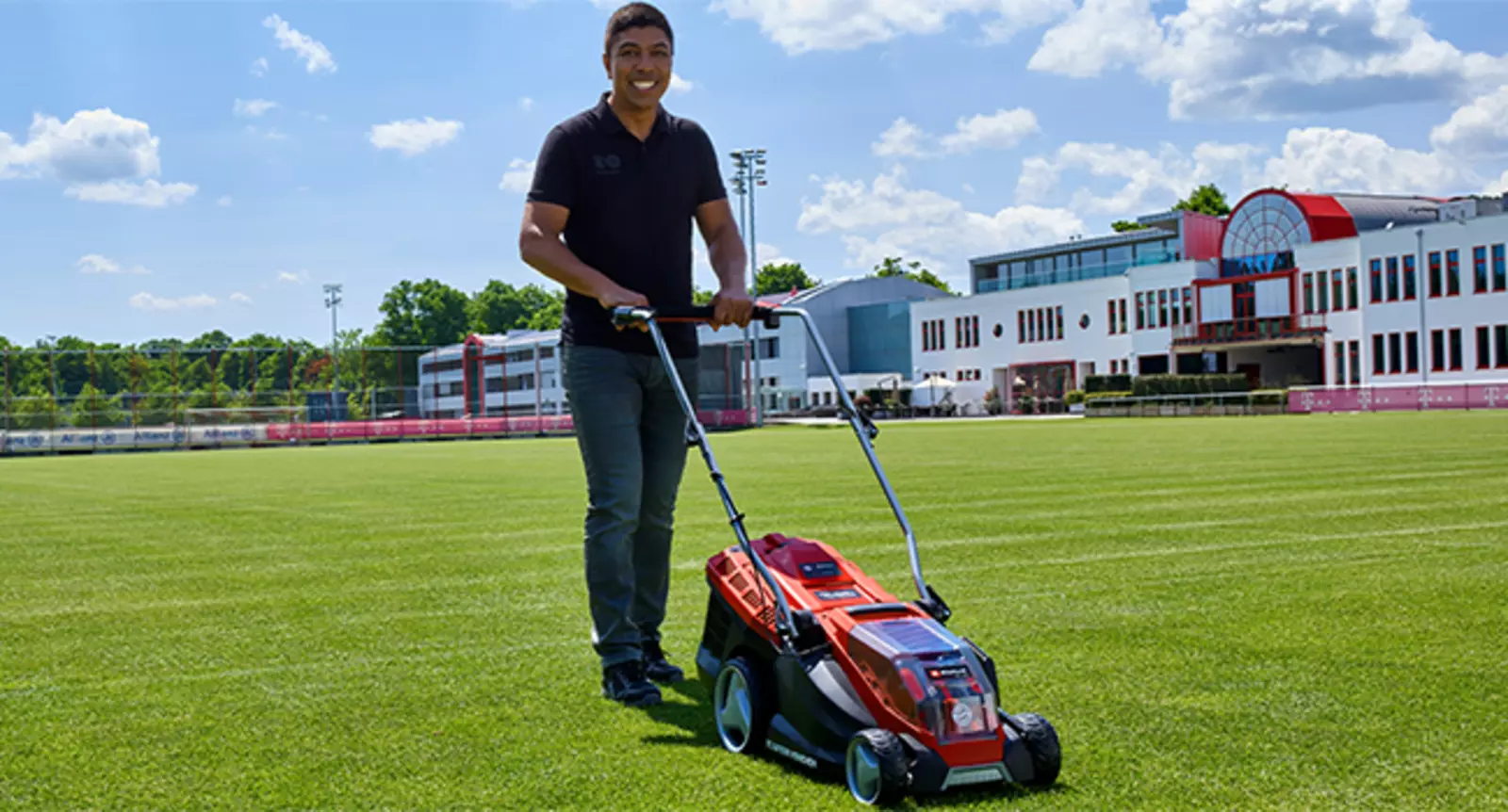 Akumulátorová sekačka Einhell GE-CM 36/36 Li Kit – FCB s logem FC Bayern v akci na fotbalovém hřišti, muž seká trávník.