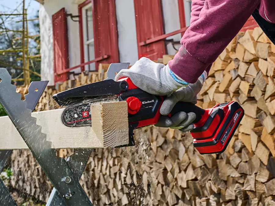 L’image montre l’élagueuse sans fil Einhell GE-PS 18/15 Li BL en train de scier un morceau de bois sur un tas de bois.