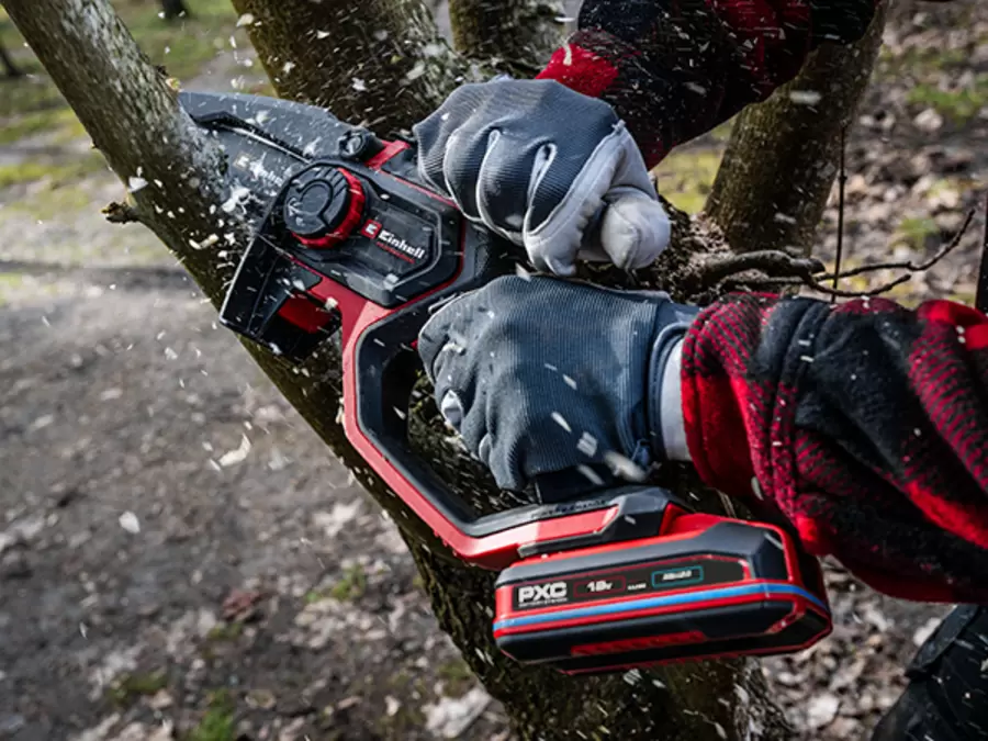 The Einhell cordless pruning chain saw GP-PS 18/20 Li BL in use on a tree. The user's protective clothing is clearly visible as is the battery.