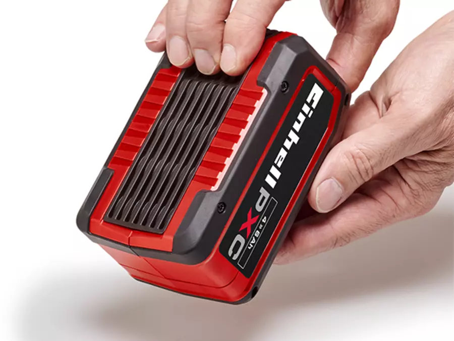 Two hands hold an Einhell Power X-Change battery at the ribbed grip section; the sturdy, rubberised housing is visible.