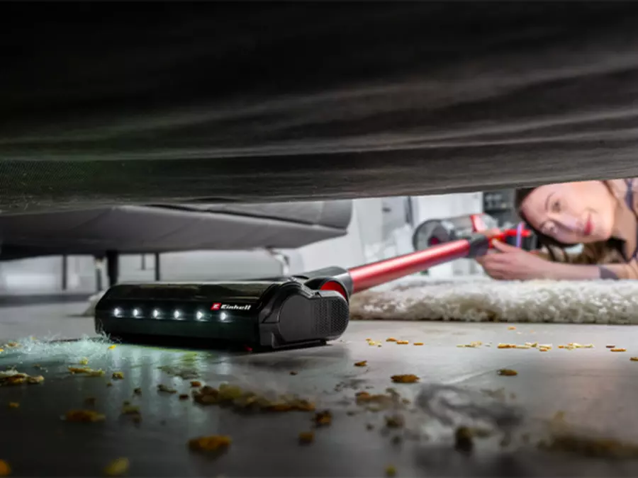 Der Einhell Akku-Stielstaubsauger TE-SV 18/270 Li BL-Solo reinigt dank flexiblem Gelenk unter einem Möbelstück.