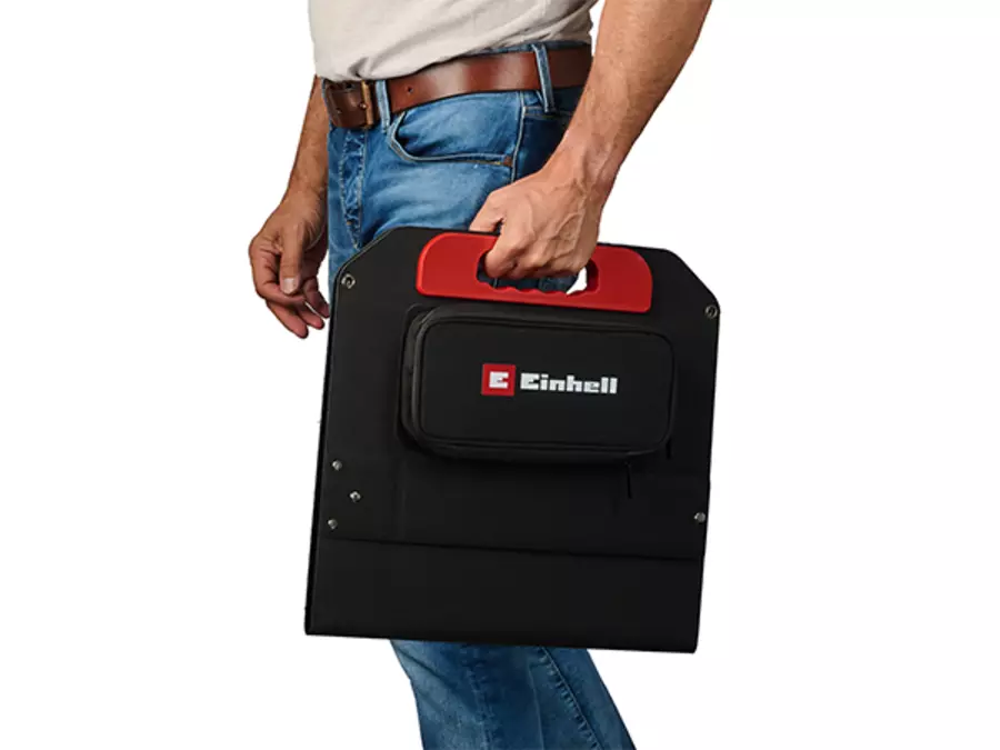 The folded Einhell solar panel is carried by a person using the carrying handle.