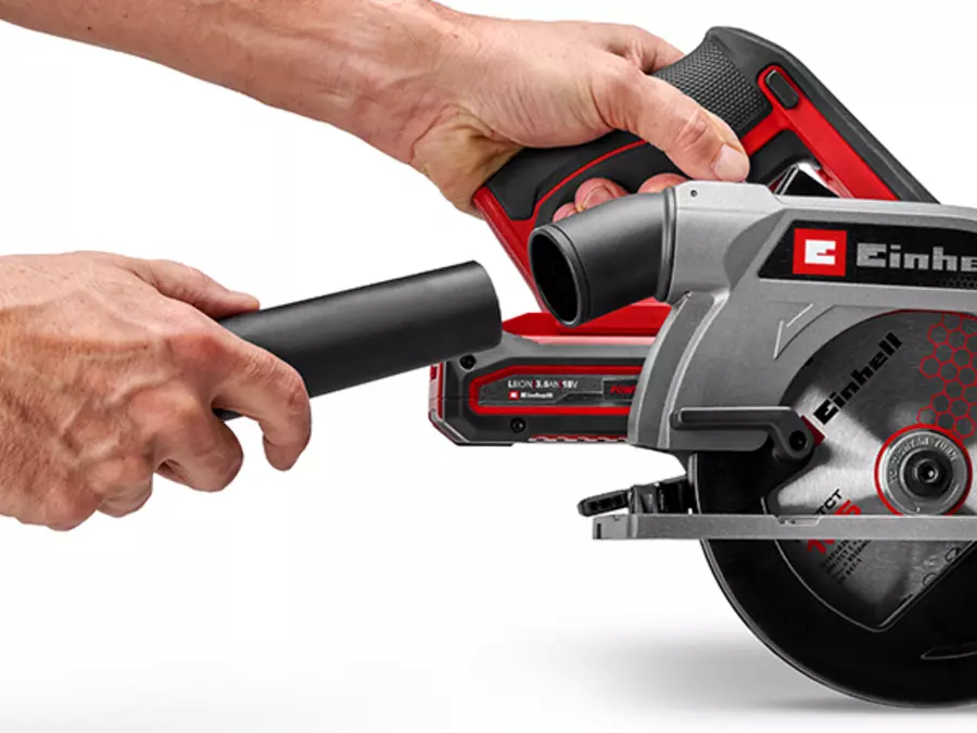 The extraction port of the Einhell Cordless Handheld Circular Saw TE-CS 18/165-2 Li - Solo being connected to a vacuum hose by a hand.