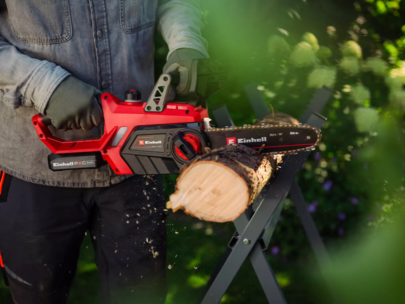 Ein Mann sägt mit der Einhell Akku-Kettensäge GE-LC 18/25-1 Li Kit (1x2,5Ah) ein Baumstück; er trägt Schutzkleidung.