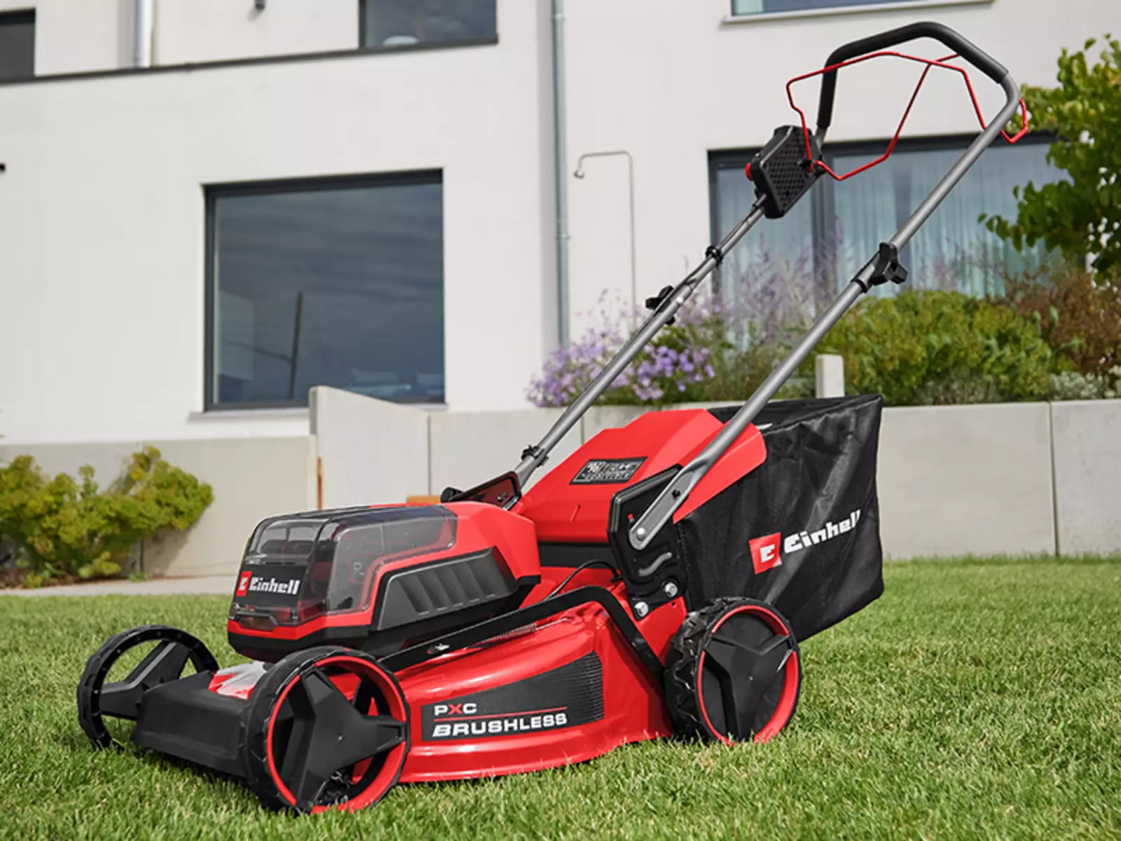 The Einhell cordless lawn mower GC-CM 36/46 S Li BL (2x 4.0 Ah) is ready for use on a lawn in front of a residential building.