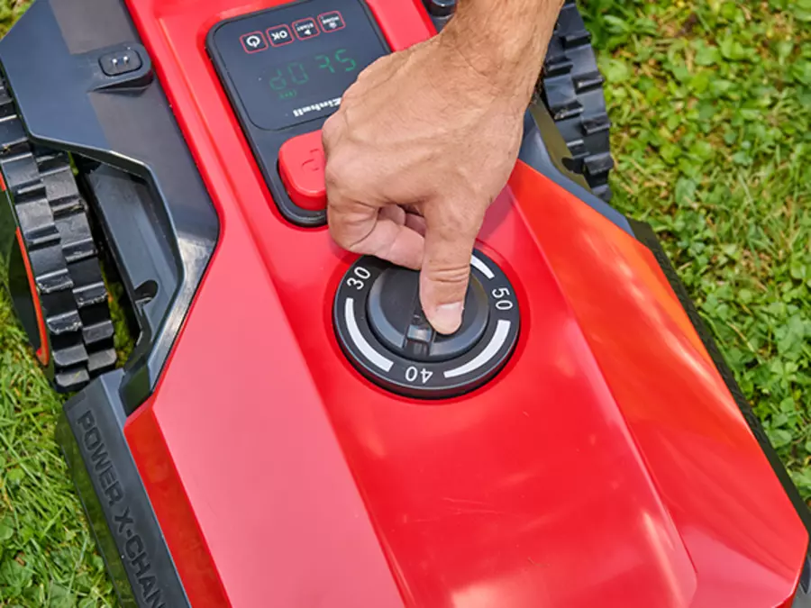 Un hombre ajusta la altura de corte con un regulador giratorio en el Einhell robot cortacésped FREELEXO 1000.