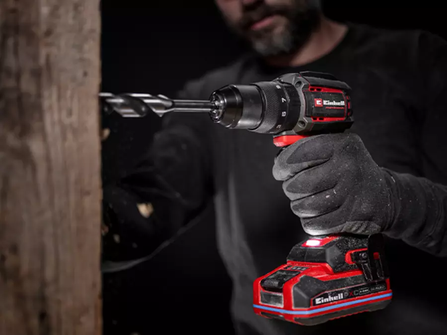 The Einhell TP-CDD 18/70 1-C Li-i +70 (3Ah) cordless impact drill/driver in use, drilling into a piece of wood, held by a person wearing gloves.