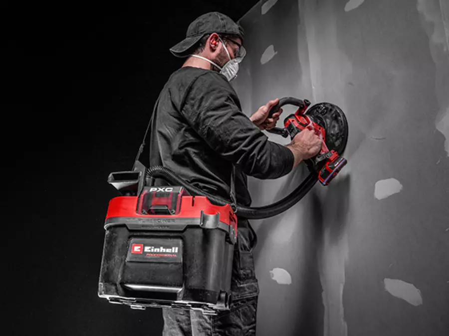 A person is wearing the Einhell Cordless Wet/Dry Vacuum Cleaner TP-VC 18/10 Li BL L-Solo with shoulder strap while working on a wall.