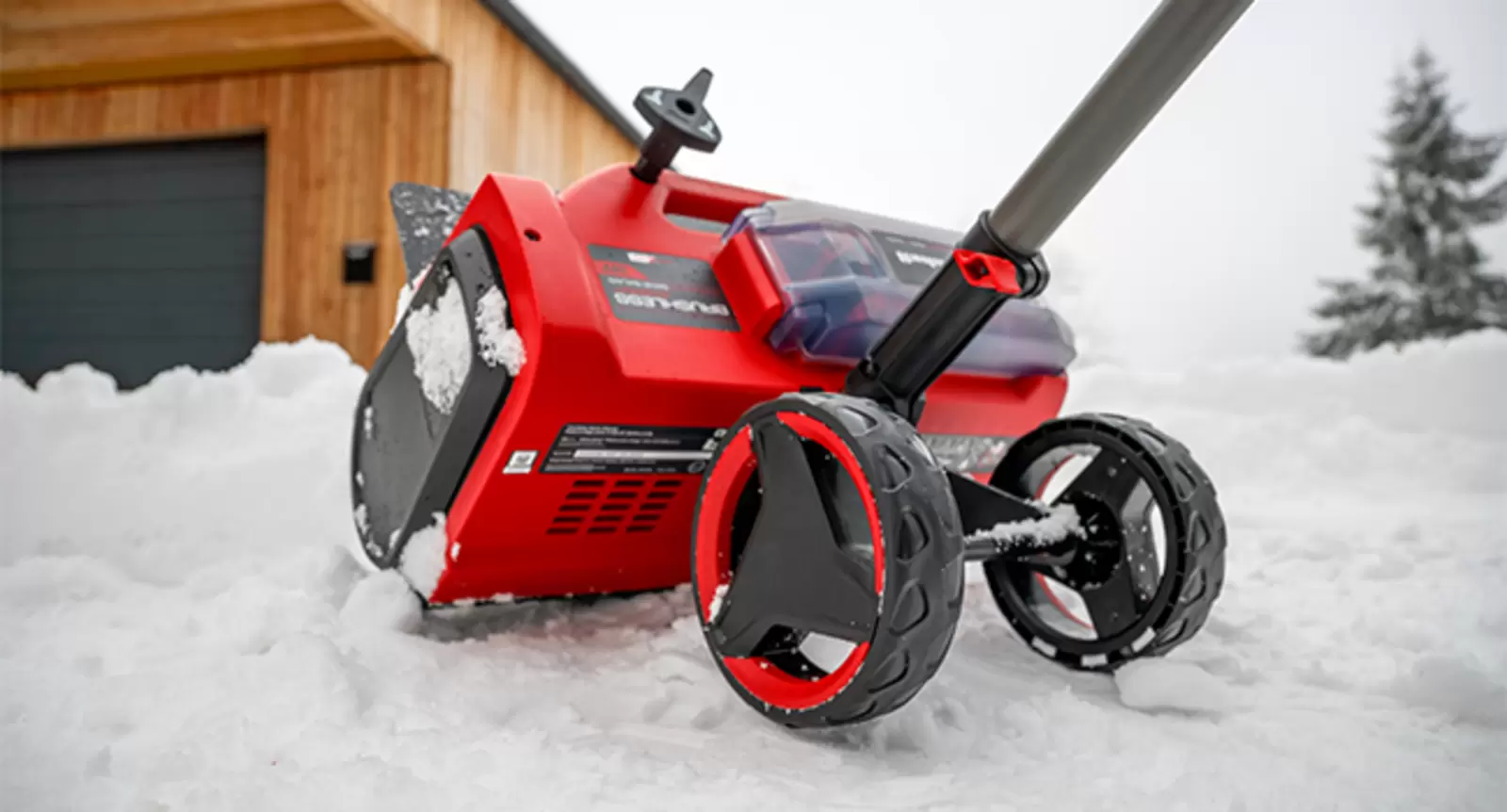 Lo spazzaneve a batteria Einhell si trova nella neve davanti a un garage.