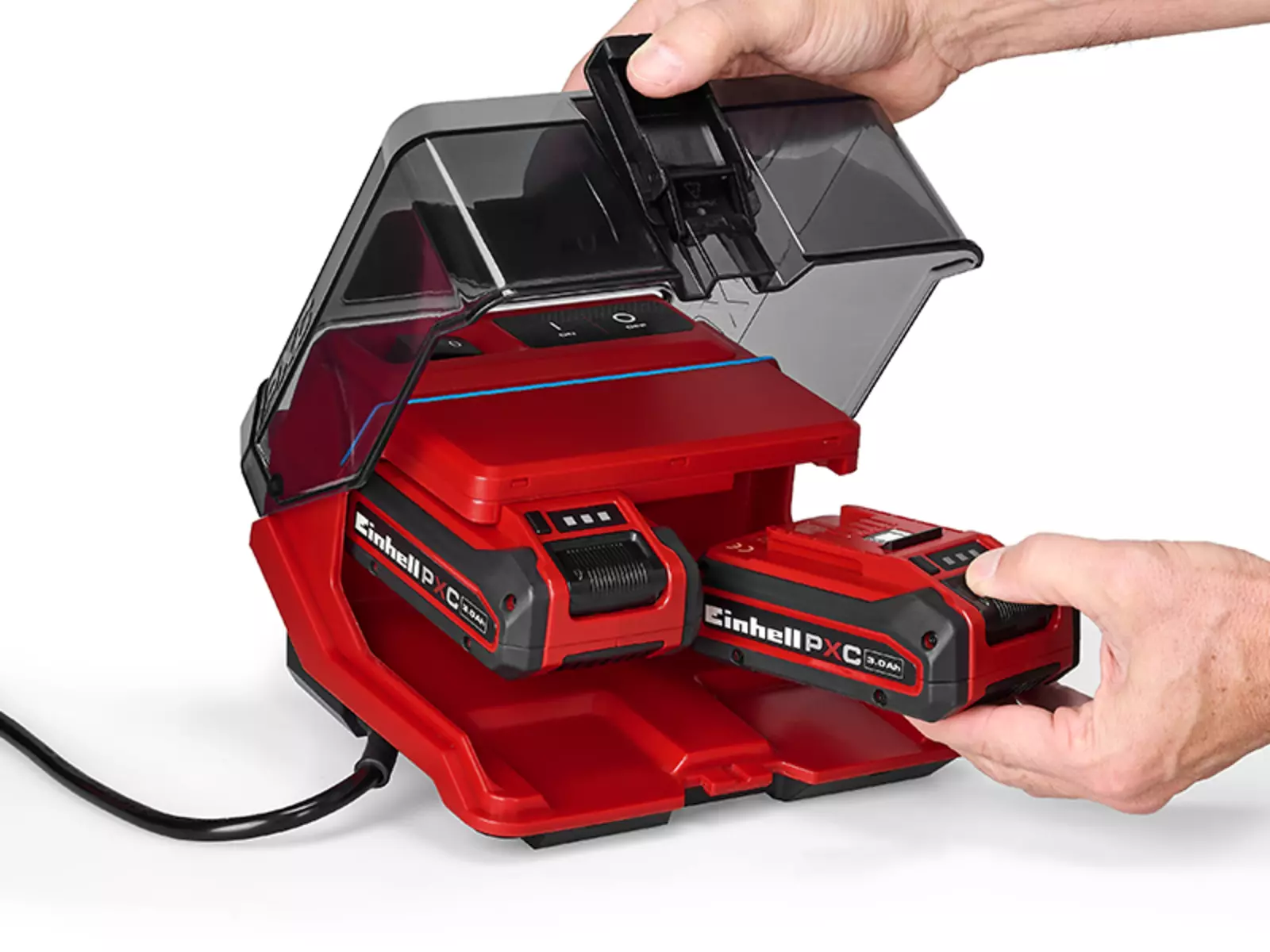 A red Einhell battery box with a hinged, transparent lid, two Power X-Change batteries inserted and a hand inserting a battery.
