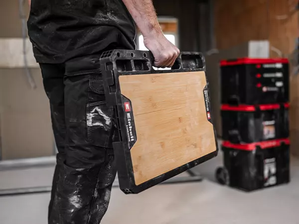 One person carries the Einhell E-Case worktop with one hand using the built-in handle.