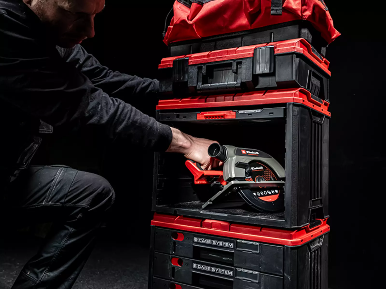 A man takes an Einhell circular saw from the open E-Case FlipFront, with additional E-Case cases and a bag stacked on top.