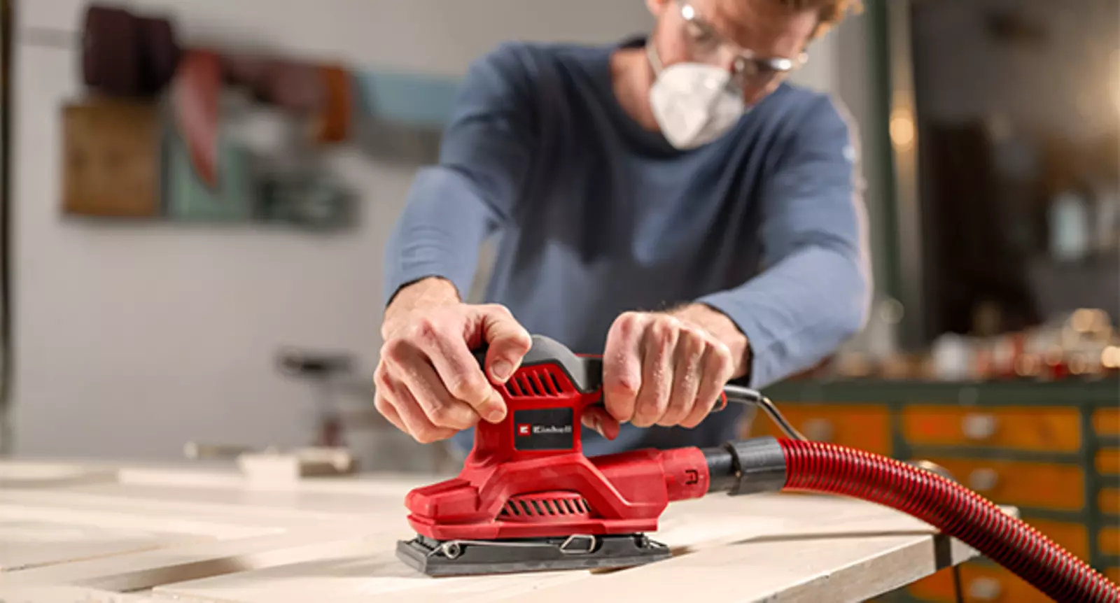 The Einhell orbital sander TC-OS 250 in red and black is used with dust extraction while sanding a wooden surface.