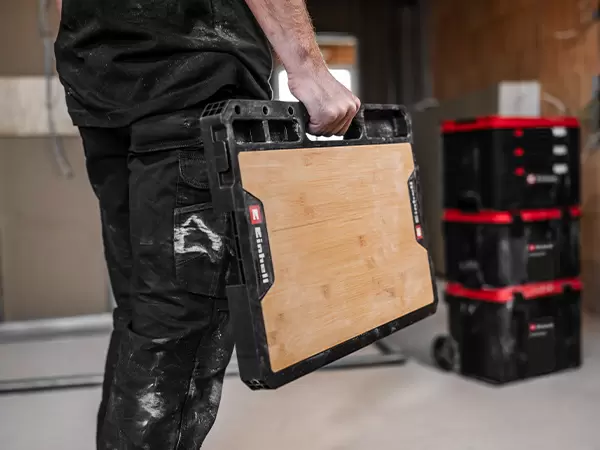 Person carrying the Einhell Pro System Work Table using the integrated carry handle.